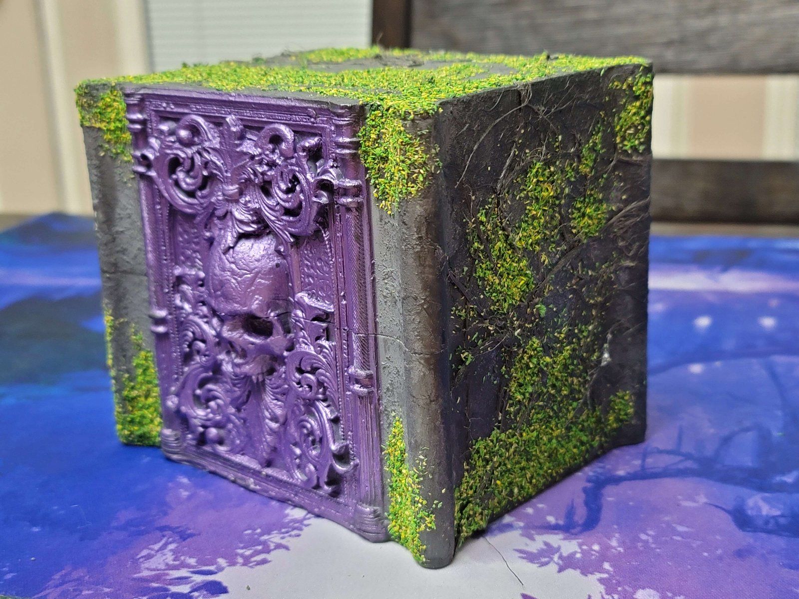 The stone deck box at an angle: the skull relief and a mossy stone side