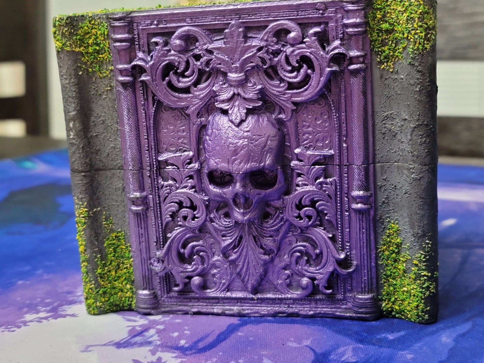 The stone deck box: a purple skull relief framed by moss